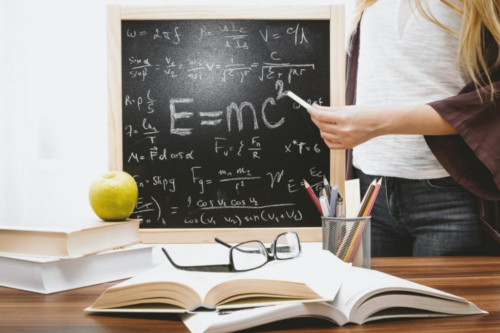 Iskolatábla képletekkel és az E=mc2 egyenlettel, előtte könyvek és szemüveg