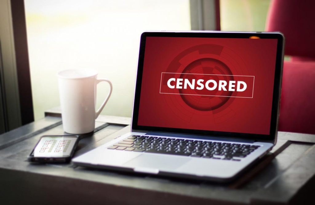 Laptop képernyőjén piros CENSORED felirat, mellette bögre és telefon
